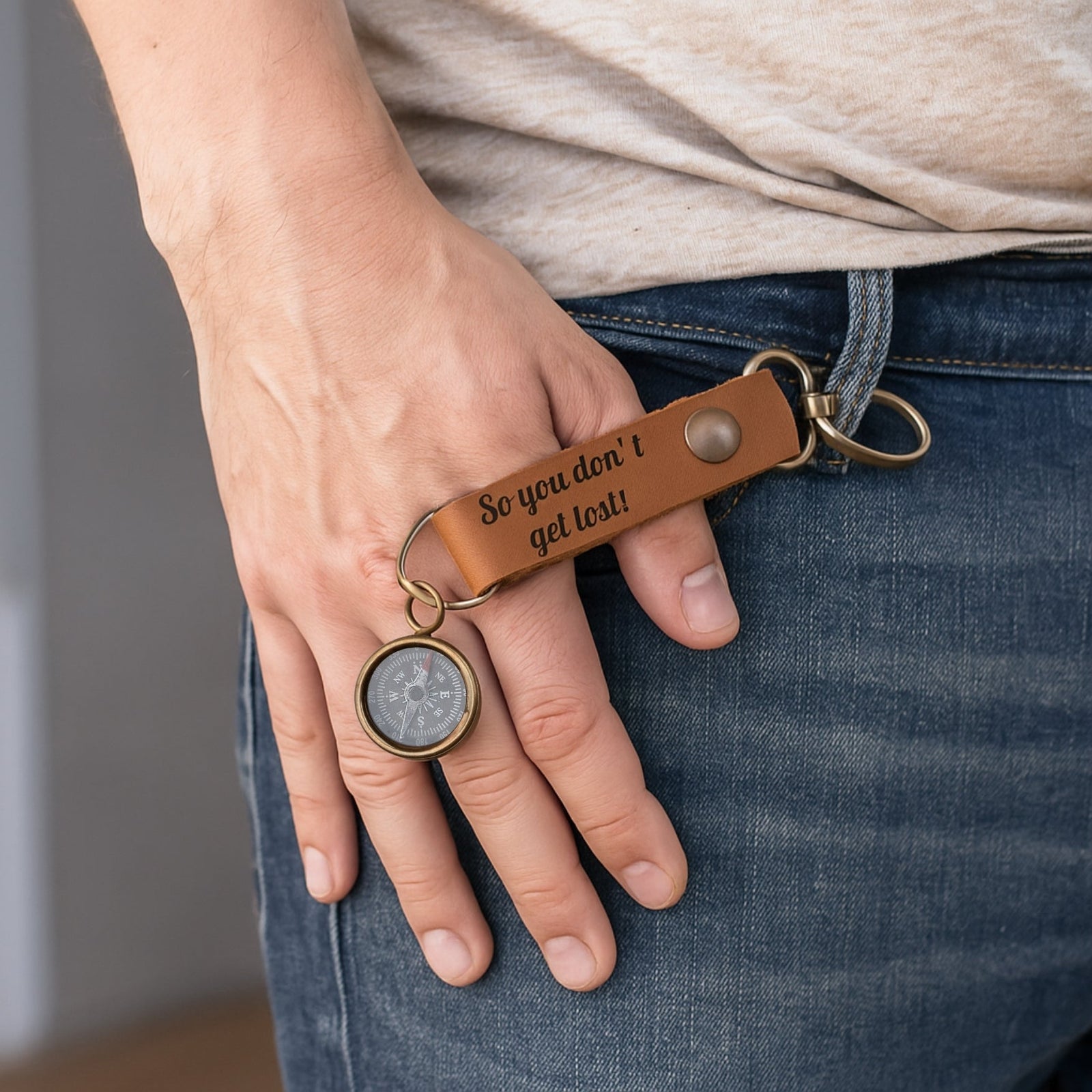 Person holding a keychain with a compass and leather tag, wearing jeans.