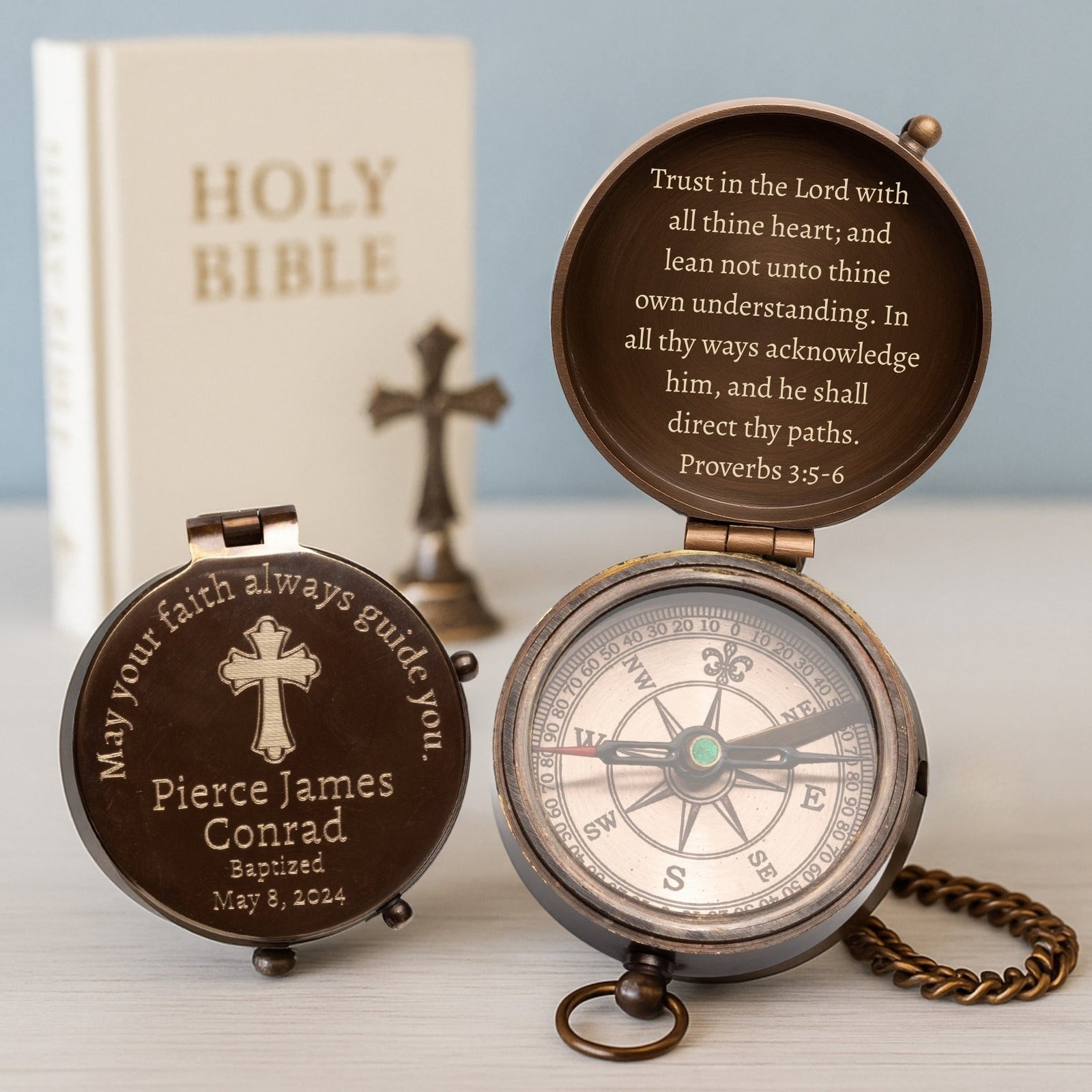 Personalized compass with engraved text and a cross, placed on a surface with a blurred background.
