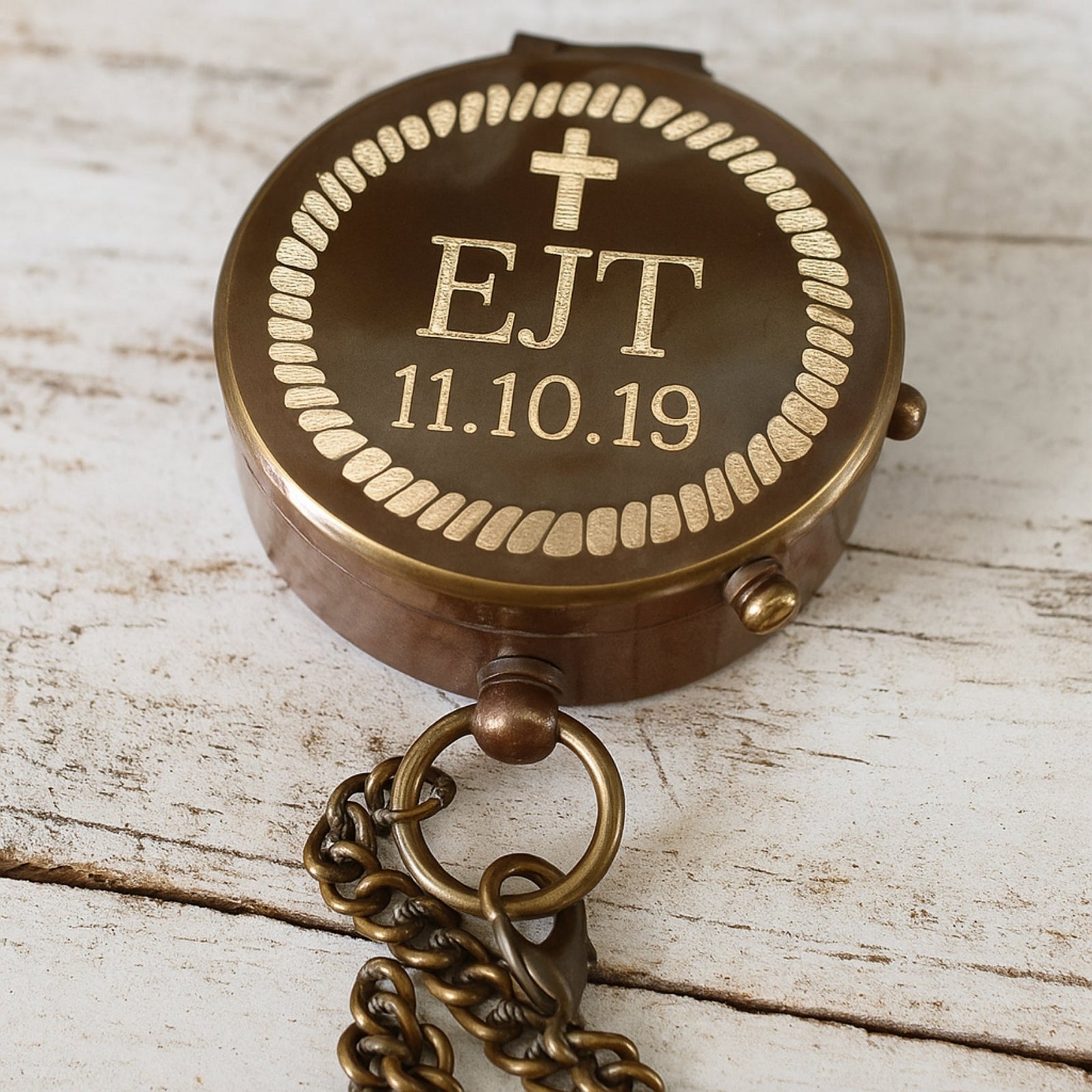 Bronze compass with engraved initials and date on a wooden surface