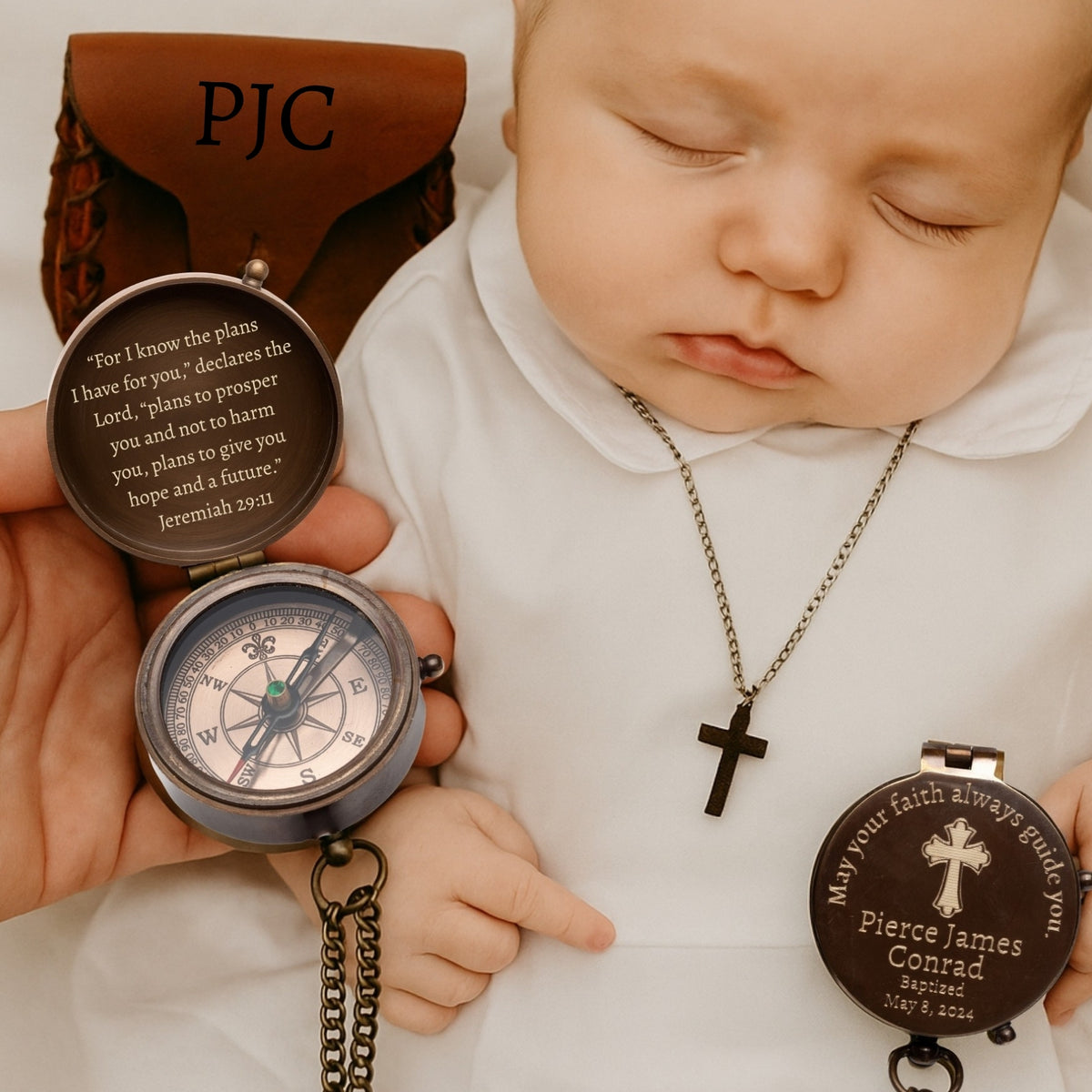 Baby holding a pocket watch with engraved text, wearing a necklace with a cross pendant.
