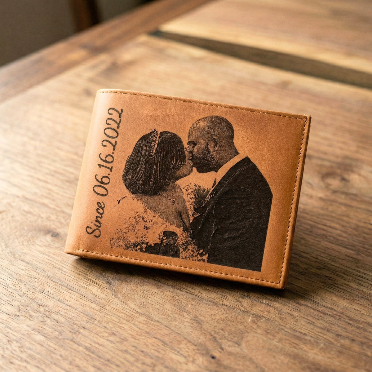 Brown leather wallet with engraved couple and date on a wooden surface