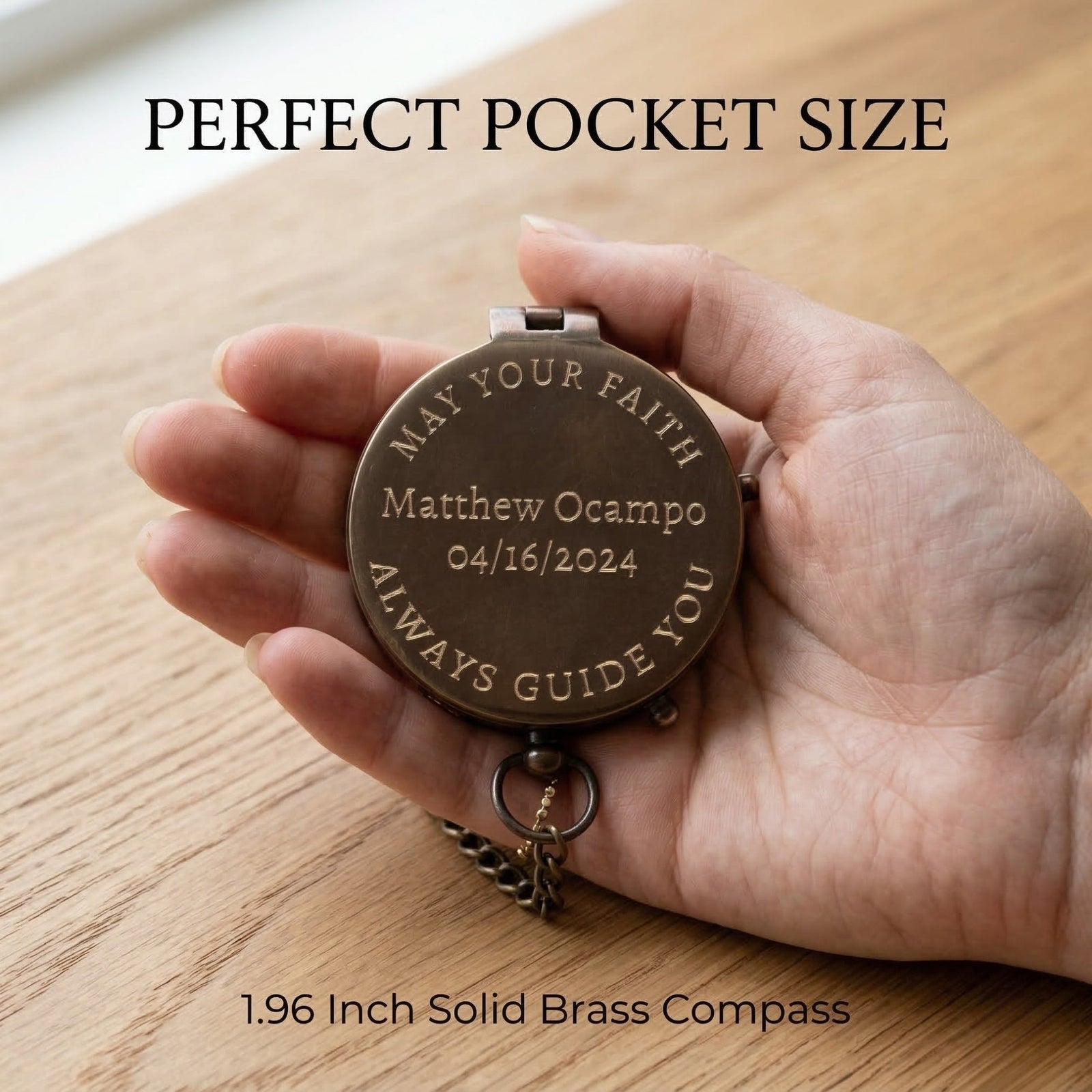 Hand holding a brass compass with engraved text on a wooden surface