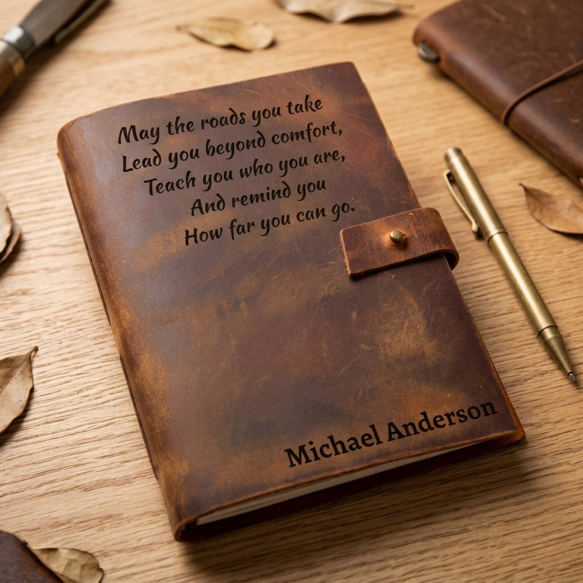 Brown leather journal with engraved text and pen on wooden surface