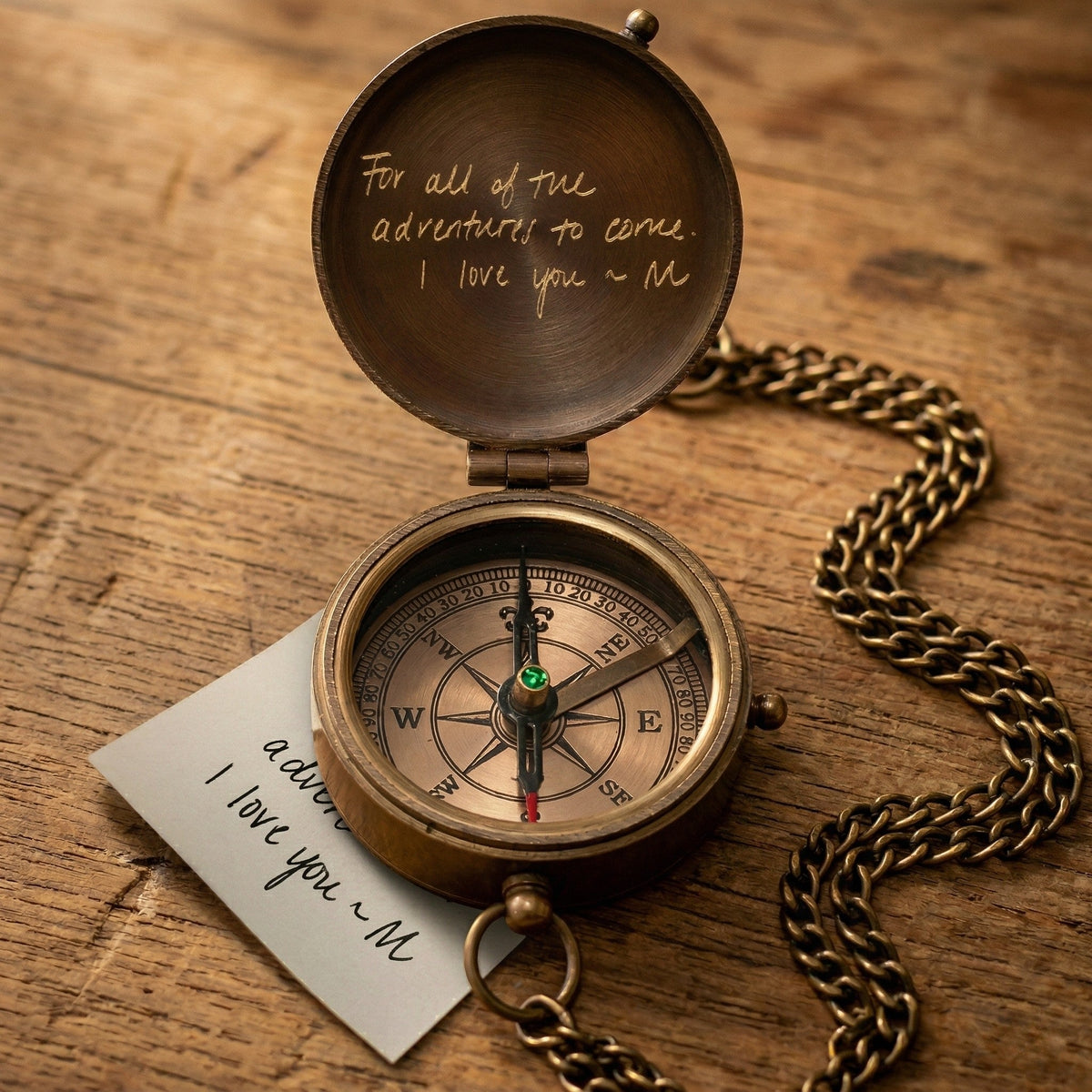 Bronze compass with chain on a wooden surface, accompanied by a card with 'I love you' message.