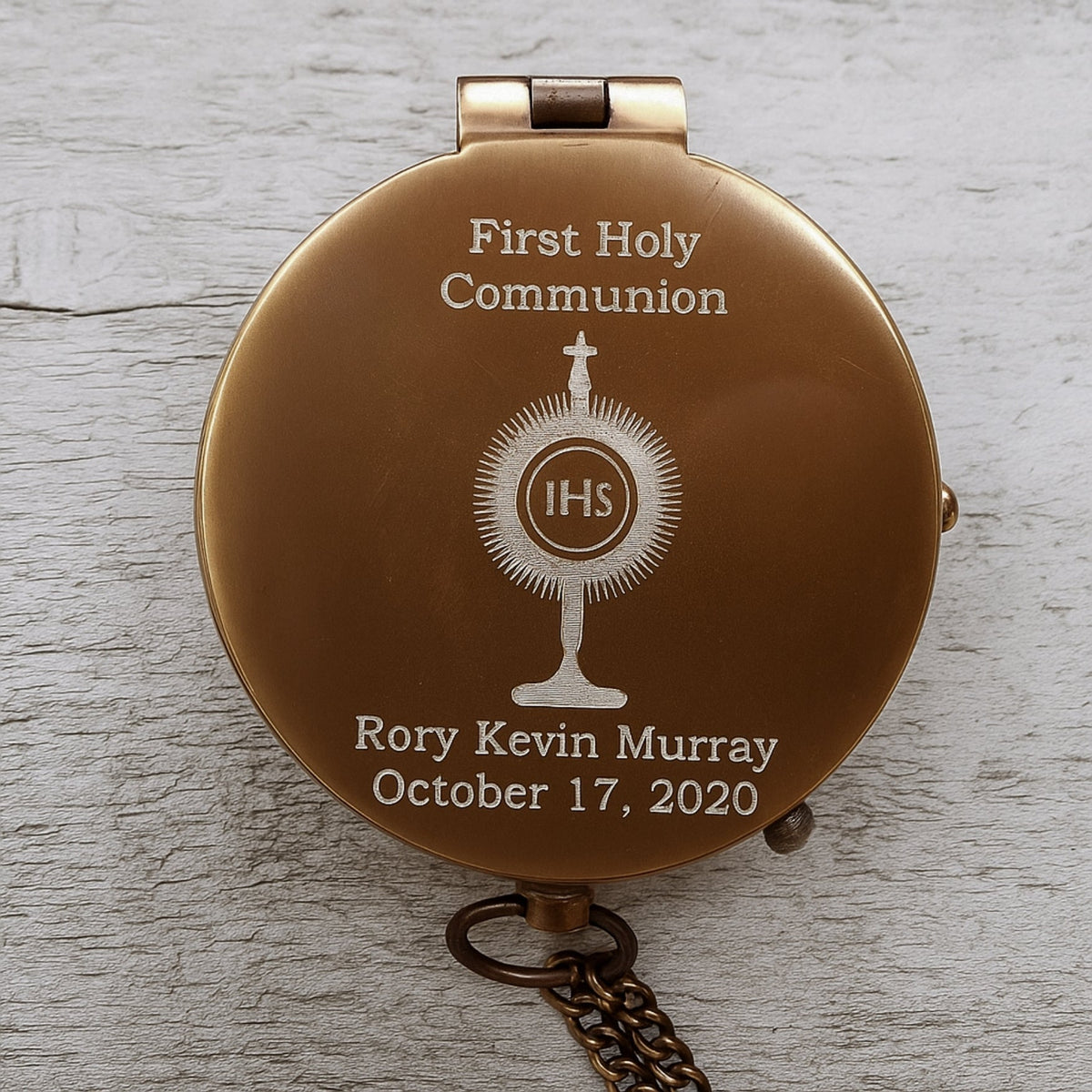 Bronze First Holy Communion pocket watch with engraved text on a wooden surface