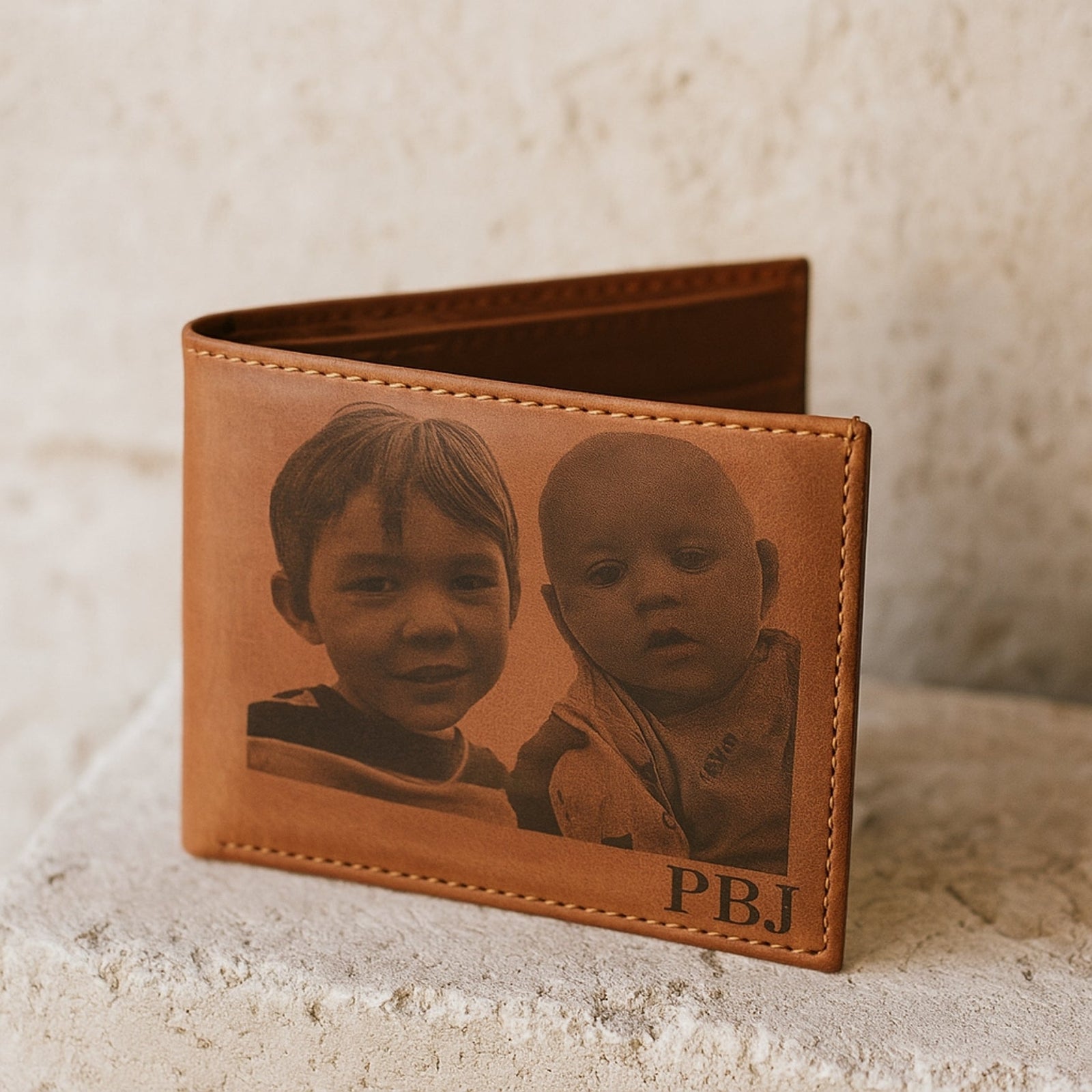 Brown leather wallet with engraved images of two children and initials on a textured surface.