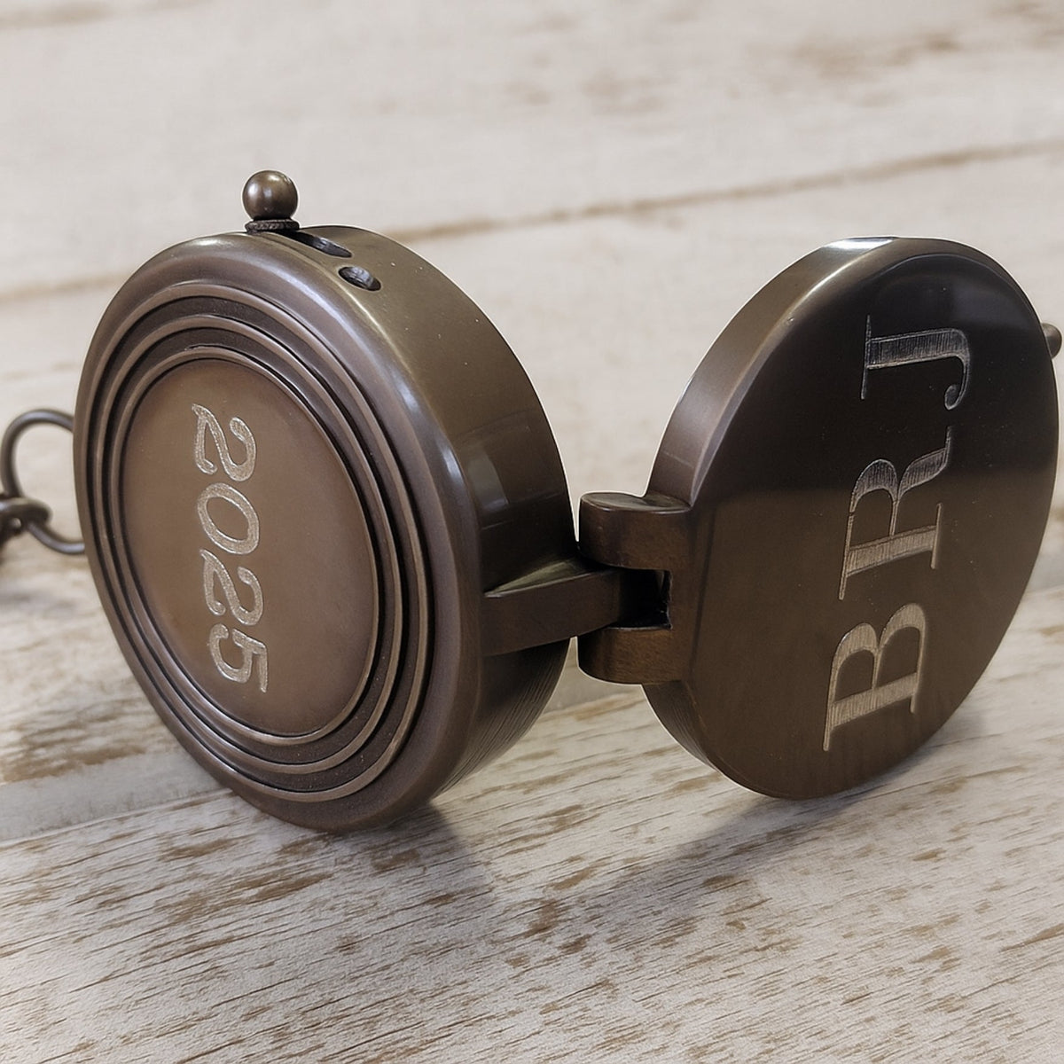 Bronze compass with &#39;BRJ&#39; branding on a wooden surface